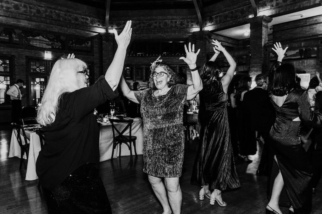 Black and white photo of two women dancing with raised arms during wedding reception at Cafe Brauer
