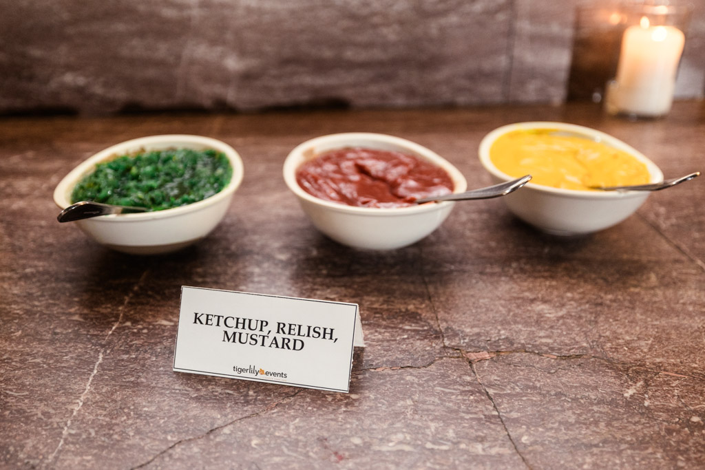 Three bowls with relish, ketchup, and mustard sit on a counter for late night hot dog service for a wedding reception at Cafe Brauer in Chicago