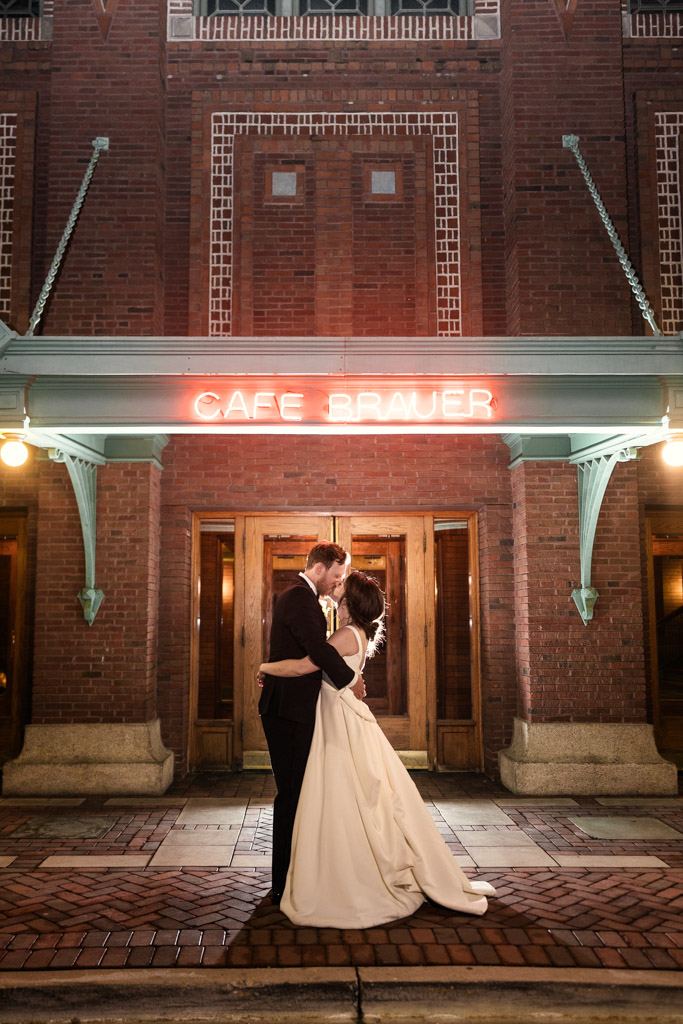Bride and groom kiss under the glowing red neon sign outside their Cafe Brauer wedding reception