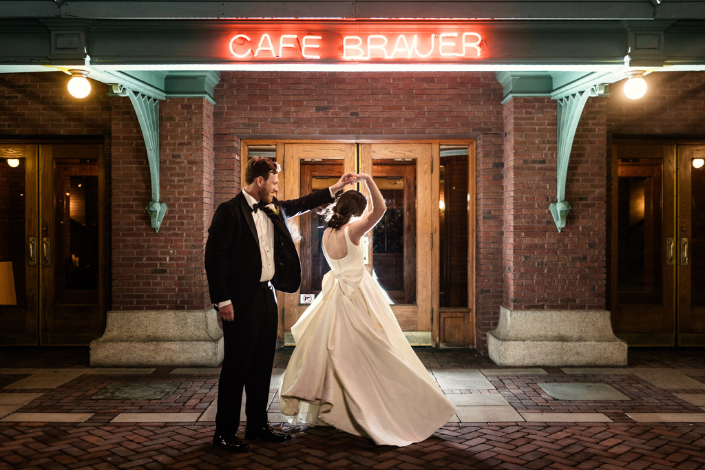 Bride and groom share a romantic dance in front of Cafe Brauer at night, illuminated by the venue's glowing red neon sign