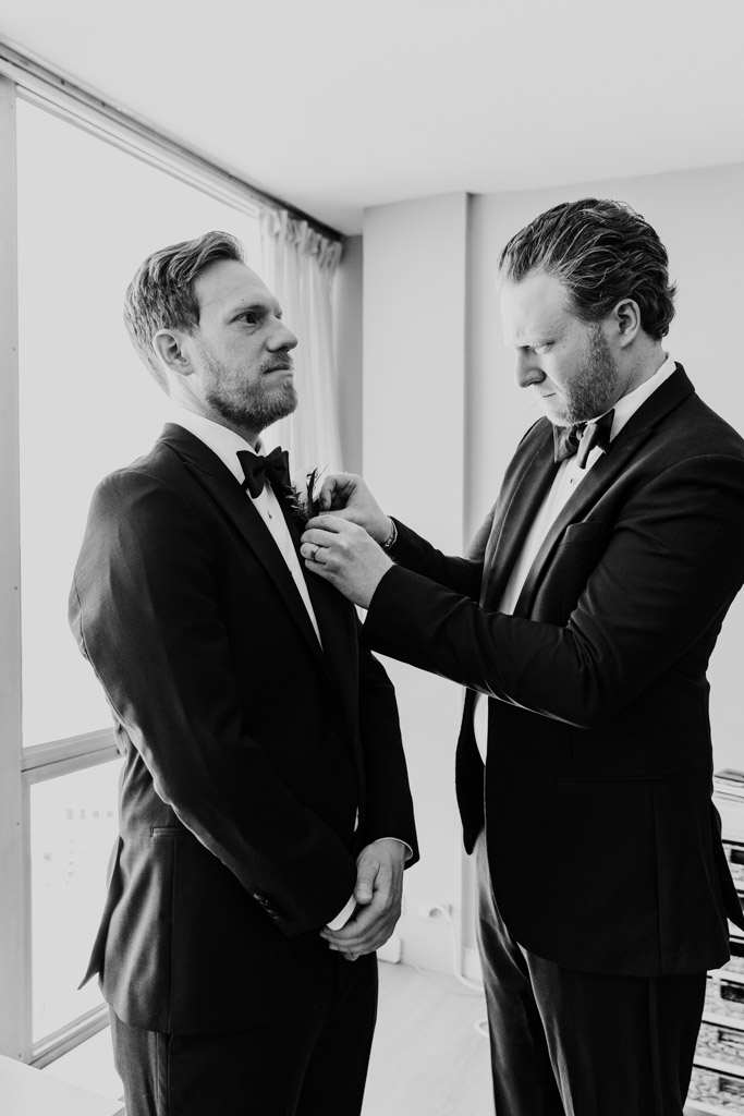 Black and white photo of Best Man adjusting the groom’s boutonniere in a bright room at the couple's apartment before their spring Chicago wedding