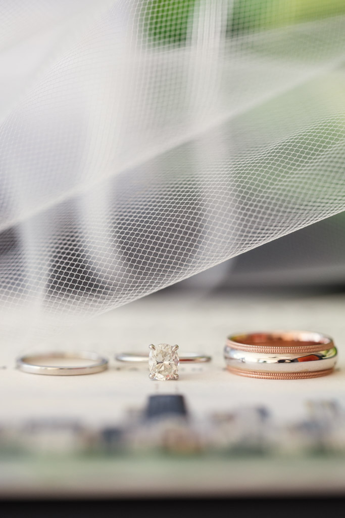 Detail photo of three wedding rings, including a diamond engagement ring under a white veil