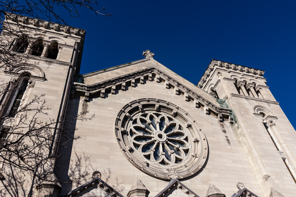 Stone facade of St. Clement Church in Chicago with a round stained glass window and two towers under a clear blue sky