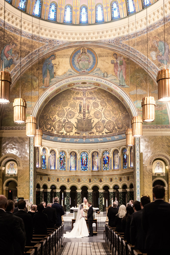 Bride and groom stand at the altar inside St. Clement Church in Chicago, with guests seated around them