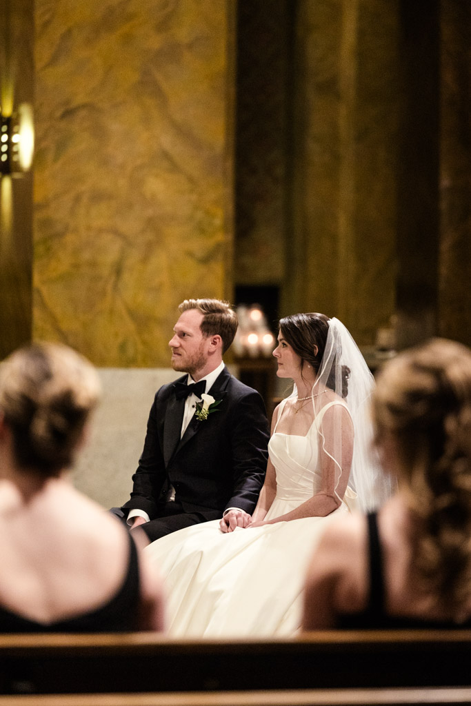 Bride and groom sit side by side in formal attire during their wedding ceremony inside St. Clement Church in Chicago