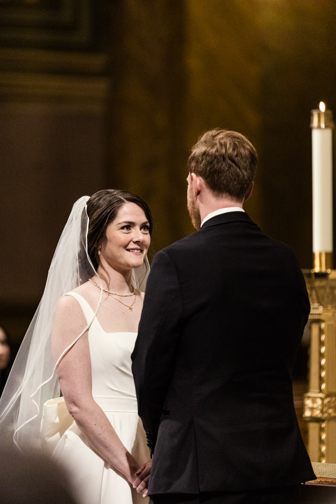 Bride and groom stand facing each other and holding hands during their wedding ceremony at St. Clement Church in Chicago