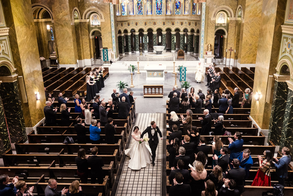 Bride and groom walk down the aisle after their wedding ceremony at St. Clement Church in Chicago as guests clap