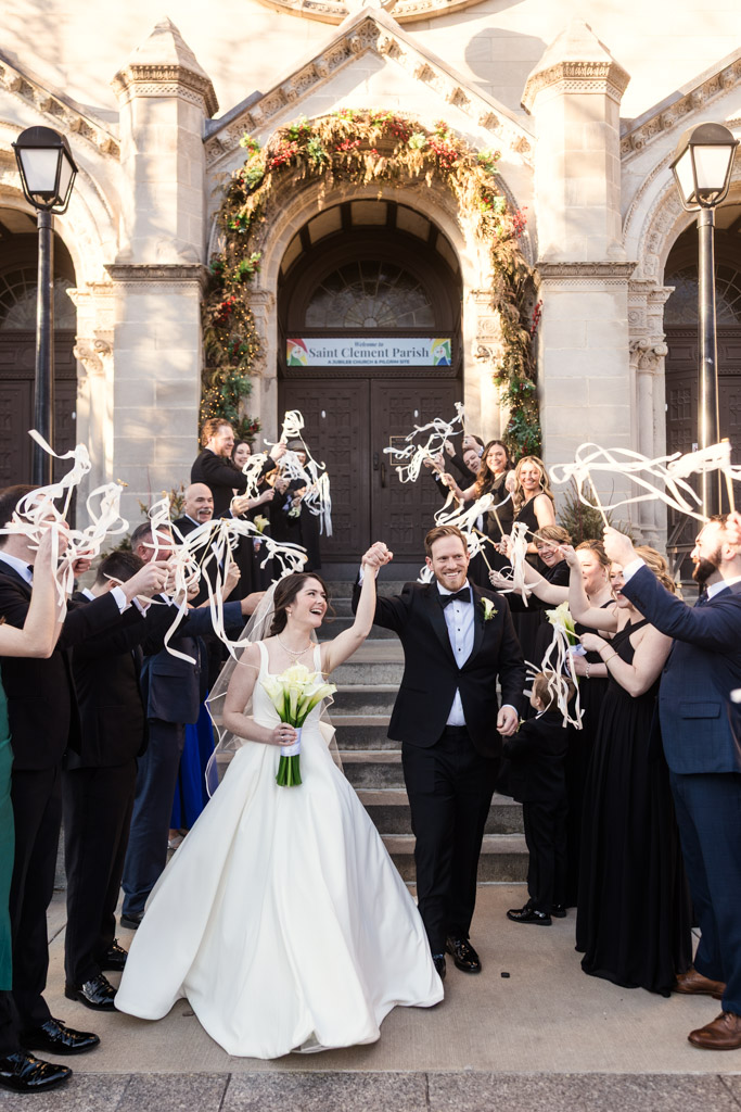 Bride and groom celebrate outside St. Clement Church in Chicago as guests wave streamers in the air