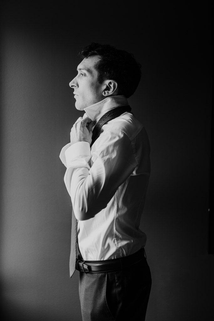 Black and white photo of groom tying his tie while getting ready at The Godfrey Hotel in downtown Chicago