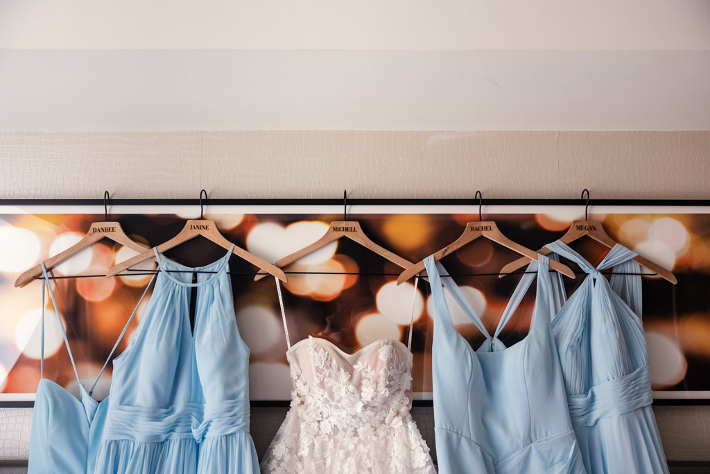 Four light blue bridesmaid dresses and one white wedding dress hanging on wooden hangers at The Godfrey Hotel in downtown Chicago