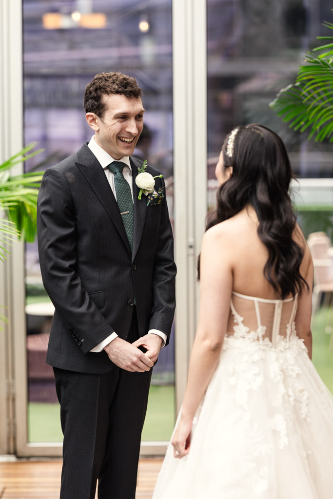 Groom in a suit smiles at his bride in a white dress during their first look at The Godfrey Hotel in downtown Chicago