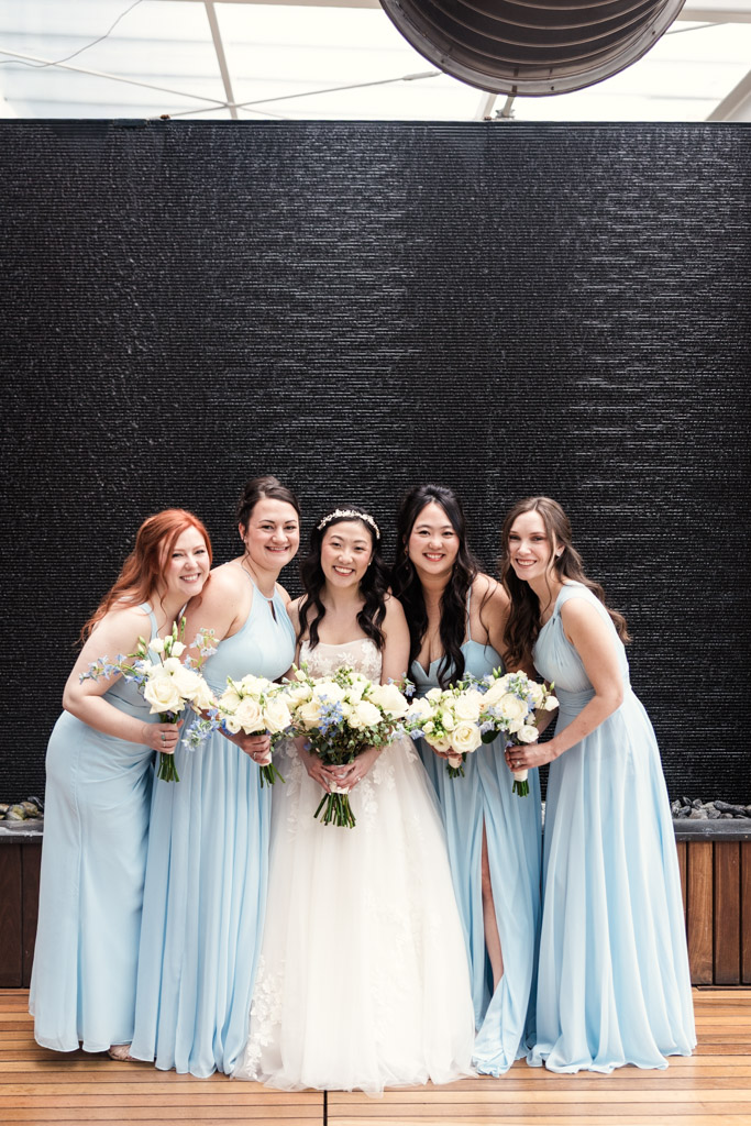 Portrait of bride in white gown and bridesmaids in light blue dresses holding bouquets at The Godfrey Hotel in downtown Chicago