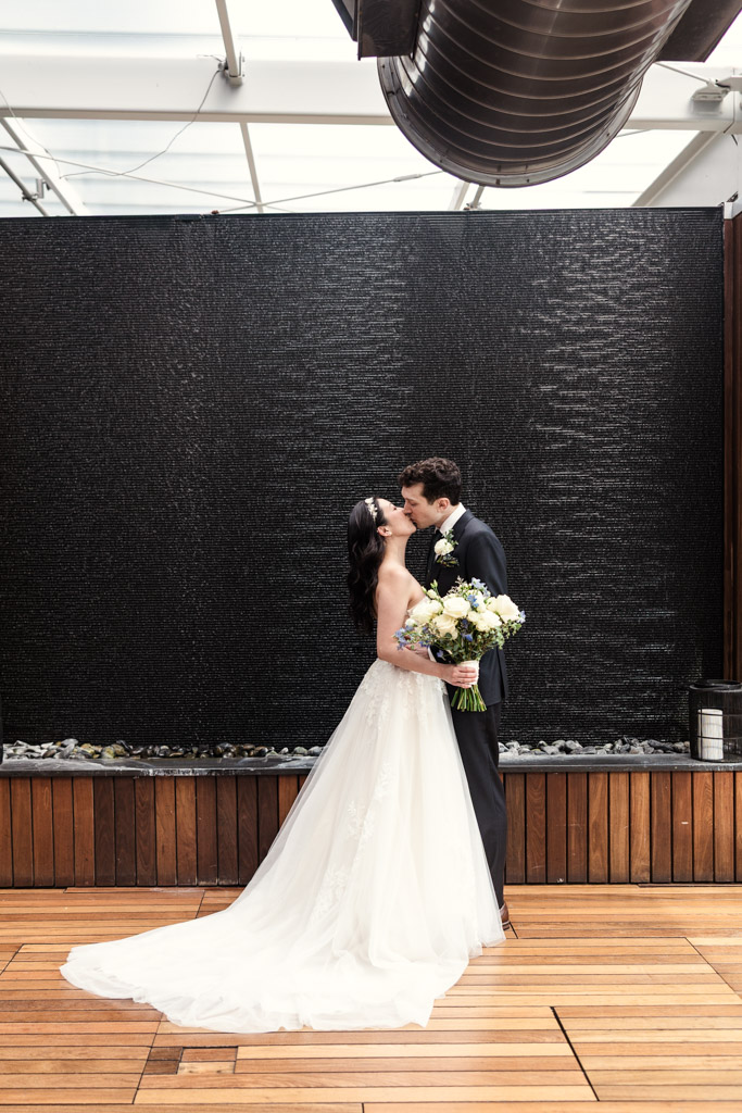 Bride and groom kiss in front of a black water feature on a wooden floor at The Godfrey Hotel in downtown Chicago