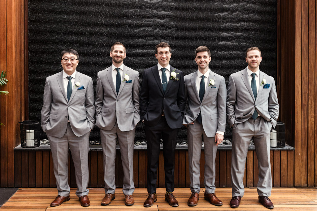 Portrait of groom and groomsmen in front of a black textured wall with wood paneling on each side at The Godfrey Hotel in downtown Chicago