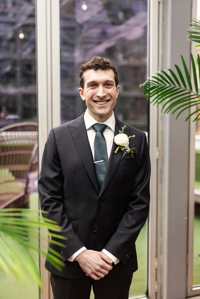 Portrait of groom beside green plants and glass doors at The Godfrey Hotel in downtown Chicago
