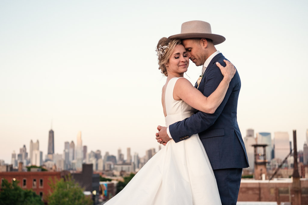 Newlyweds embrace on the rooftop of The Hive on Hubbard with Chicago skyline in the background at sunset