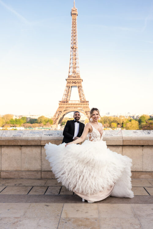 Bride and groom posing joyfully in front of the Eiffel Tower on a sunny day.