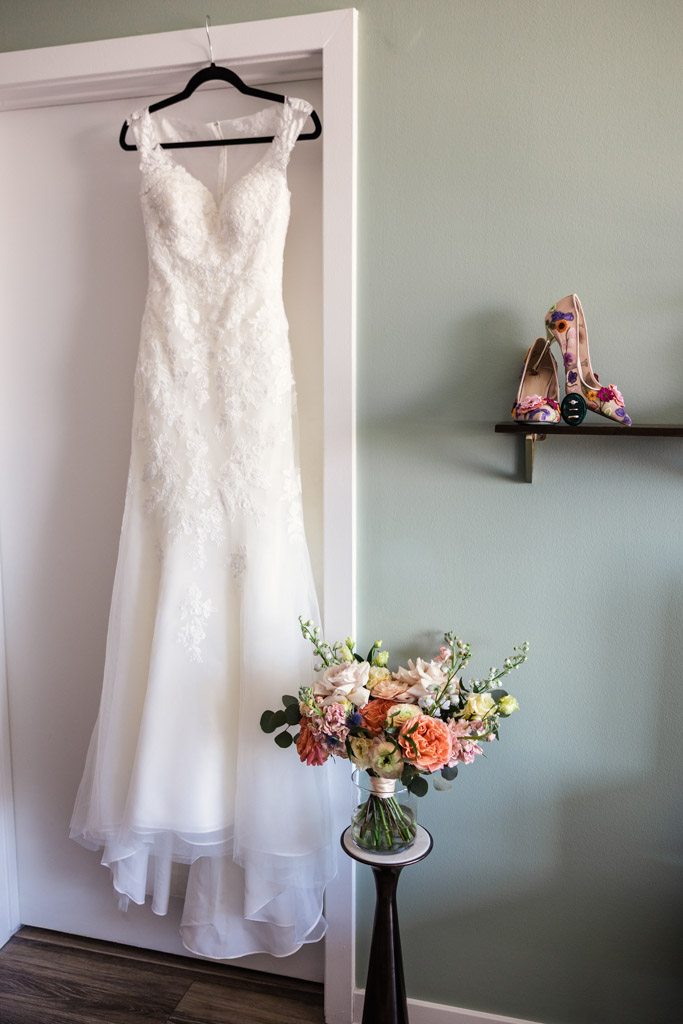 Bride's wedding dress on a hanger, with floral heels on a shelf and bouquet on a small table nearby for wedding ceremony at Ada Street Chicago