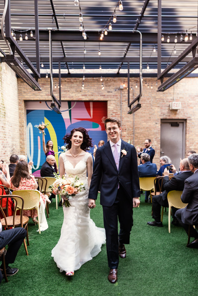 Bride and groom smiling and holding hands as they walk down the aisle during their wedding ceremony at Ada Street Chicago