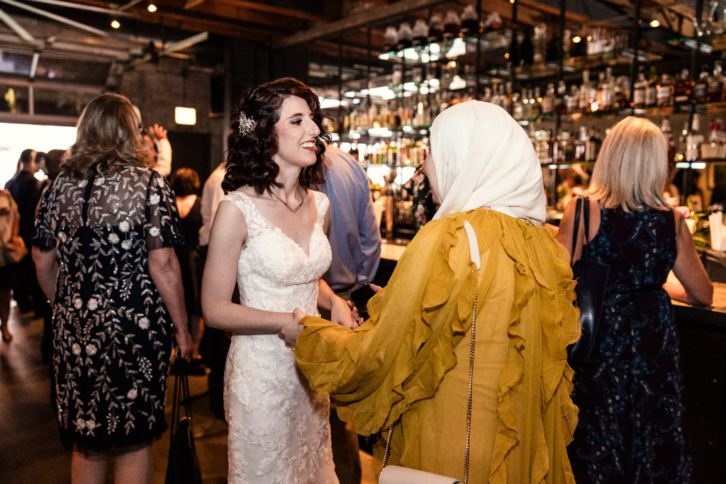 A bride in a white dress smiles and holds hands with a guest in a yellow outfit during Ada Street Chicago wedding reception