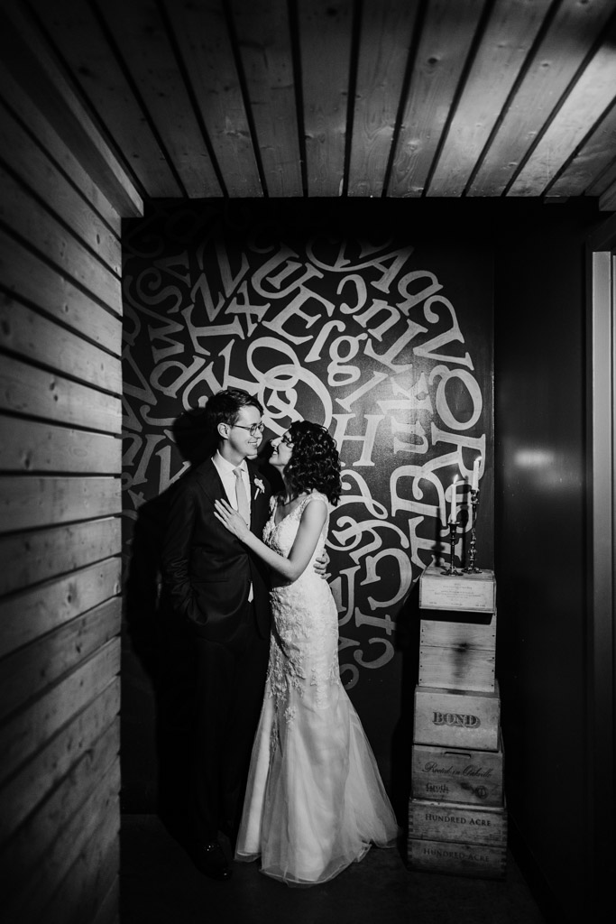 Black and white photo of bride and groom stand closely together in front of a wall with abstract letters at Ada Street Chicago