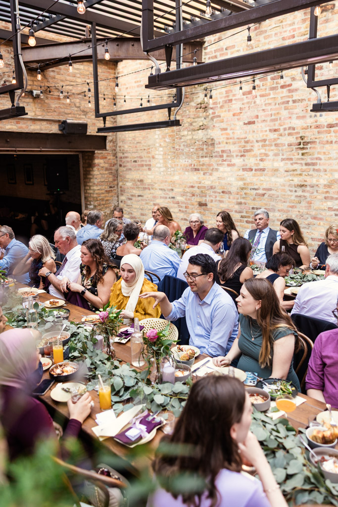 Guests sit at long tables enjoying a meal together during Ada Street Chicago wedding reception
