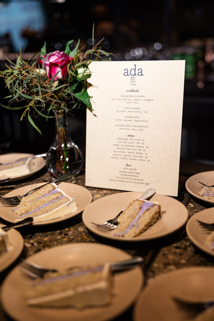 Slices of cake on plates with forks, set beside a menu and a vase with a pink rose and greenery at Ada Street Chicago wedding reception