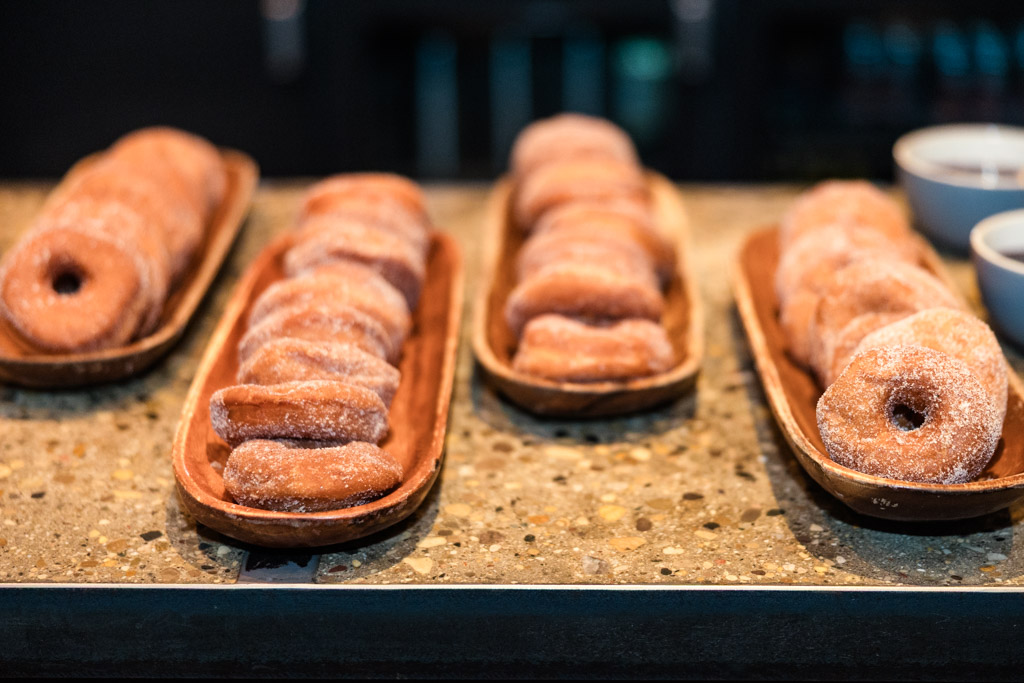 Four wooden trays filled with sugar-coated donuts sit on a speckled countertop for Ada Street Chicago wedding reception