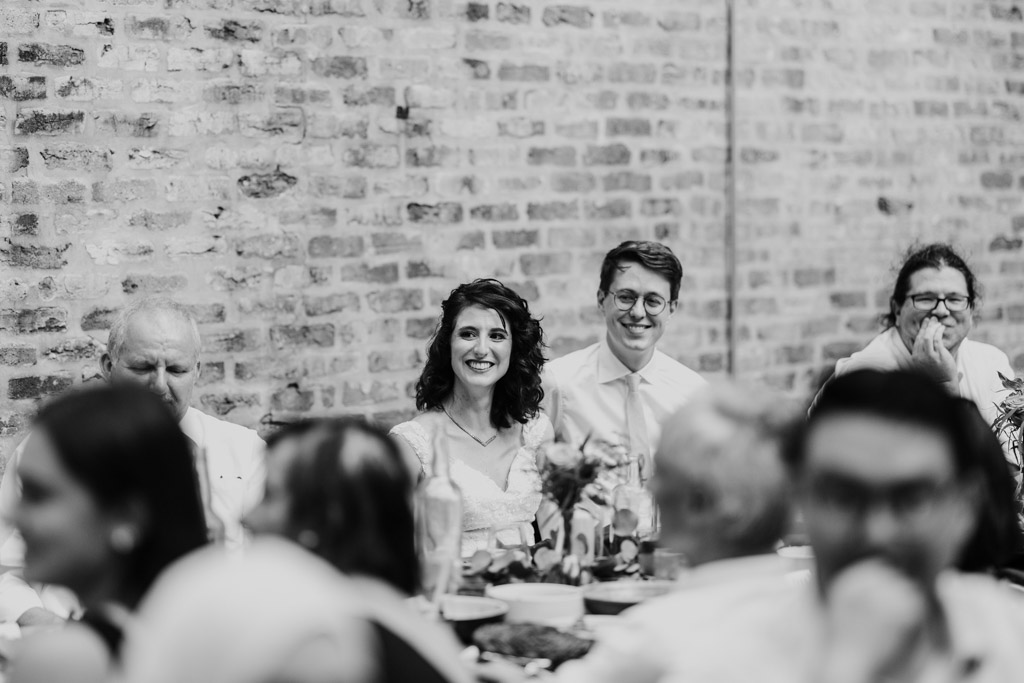 Black and white photo of newlyweds sitting at a table during a wedding reception speech at Ada Street Chicago
