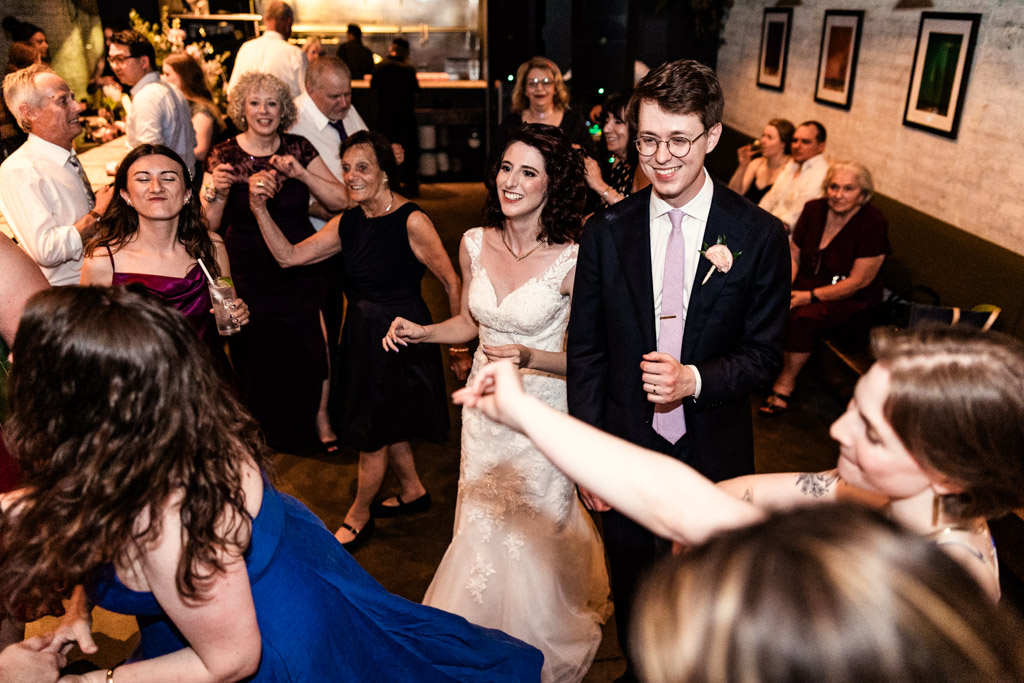 Bride and groom smile and dance surrounded by guests during wedding reception at Ada Street Chicago