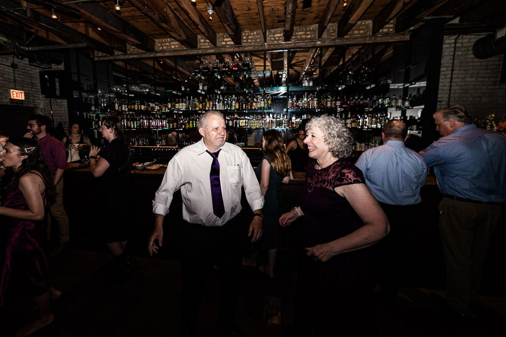 Bride's parents smile and dance together inside Ada Street Chicago while other guests mingle in the background