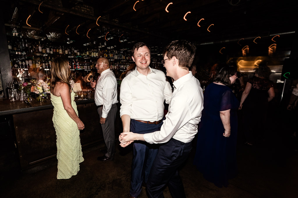 Groom and guest dance together joyfully during wedding reception at Ada Street Chicago, with other guests mingling in the background