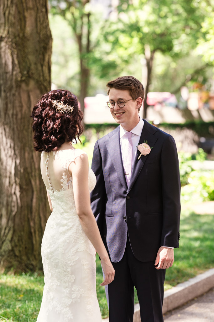Bride and groom smile at each other outdoorsduring their first look in downtown Chicago surrounded by lush greenery on a sunny day