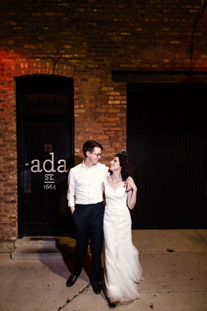 Bride and groom smile at each other while standing outside Ada Street Chicago at night