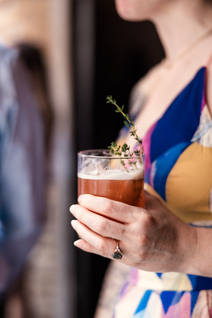 A woman in a colorful dress holds a custom cocktail garnished with a sprig of thyme at Ada Street Chicago