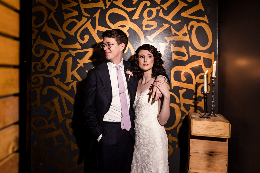 Creative portrait of bride and groom looking in different directions standing together in front of a golden letter mural at Ada Street Chicago