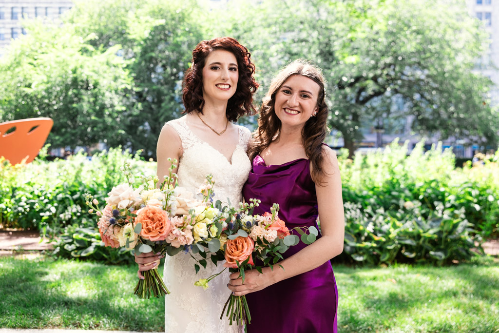Portrait of bride in white and Maid of Honor in purple, holding bouquets of flowers