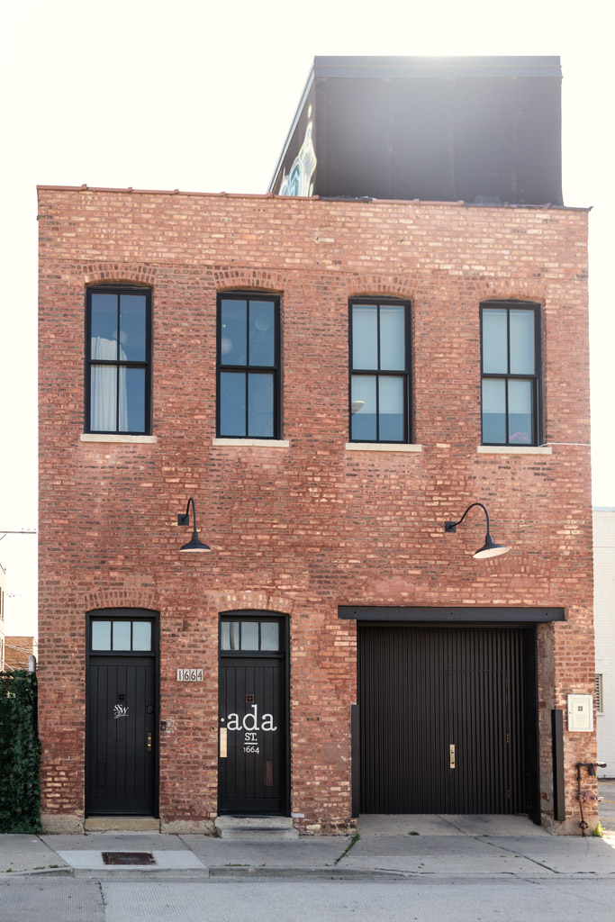 Exterior of Ada Street Chicago, featuring black doors, large windows, and industrial-style wall lamps