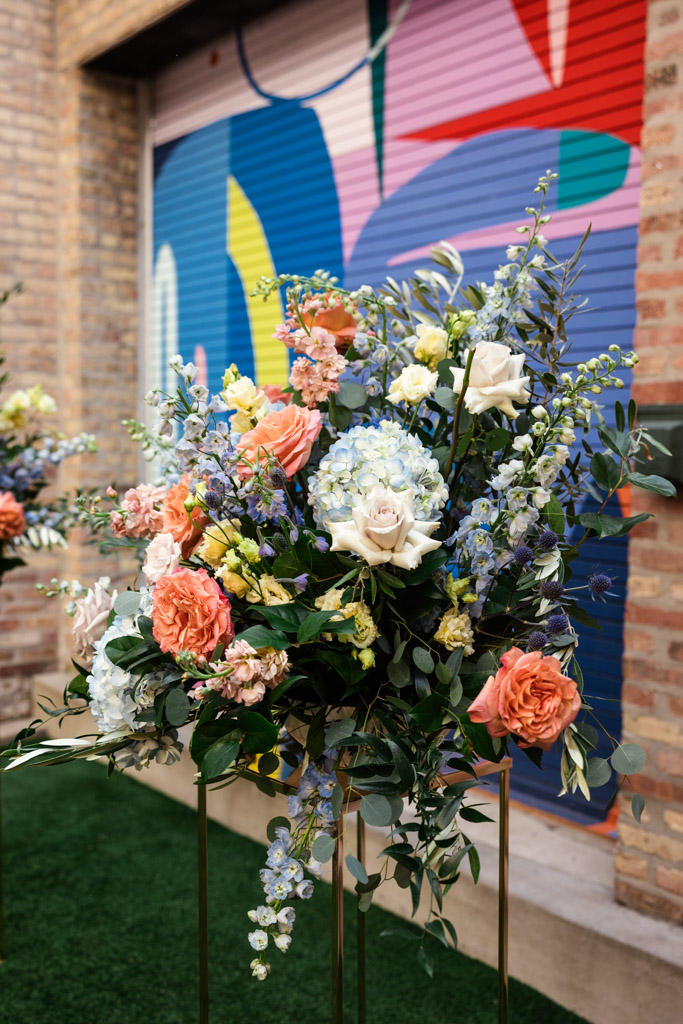 Colorful flower arrangement with roses and hydrangeas displayed in front of a vibrant, abstract mural on a brick wall inside Ada Street Chicago