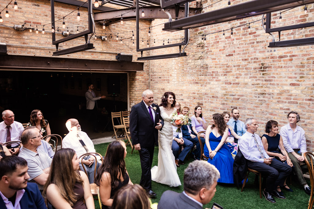 A bride walks down the aisle with her father during Ada Street Chicago wedding ceremony, guests seated on either side watching
