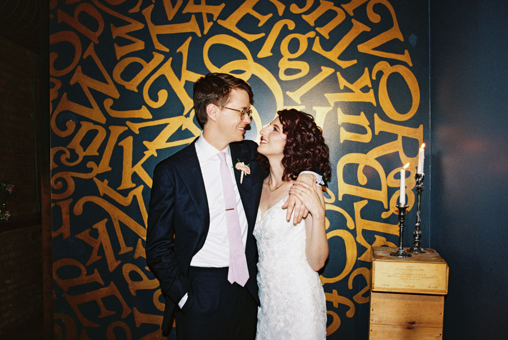 A bride and groom smile at each other in front of a gold-lettered wall and a lit candle at Ada Street Chicago.
