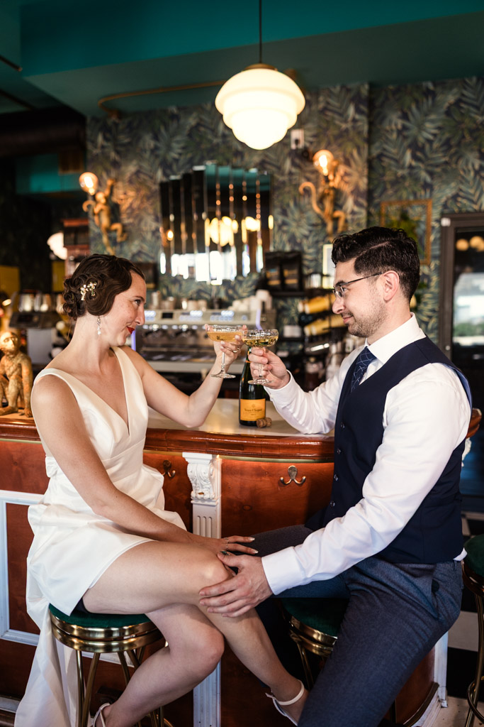 Woman and her partner toast with champagne while sitting together at the bar during Cafe Deko engagement session