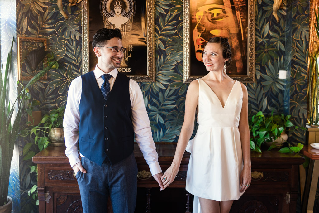 Engaged couple holding hands and smiling, standing in a stylish, plant-filled room with patterned wallpaper and framed art at Cafe Deko in Chicago