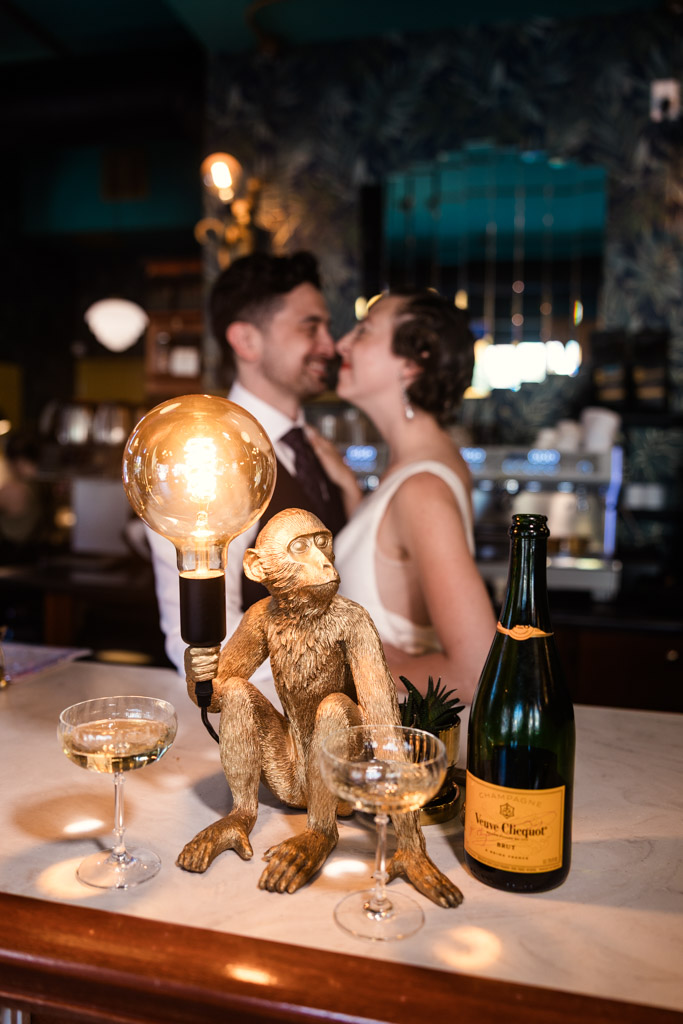 Creative photo of engaged couple standing near the bar inside Cafe Deko in Chicago with a monkey lamp, and two filled glasses in the foreground