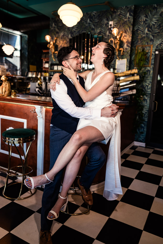 Engaged couple laughs together at Cafe Deko in Chicago; she sits on his lap in a white dress and he smiles at her