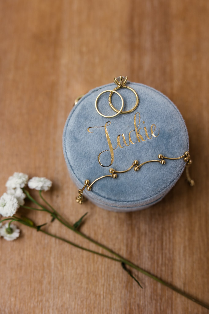 Gold rings and bracelet rest on a blue velvet box with small white flowers on wood