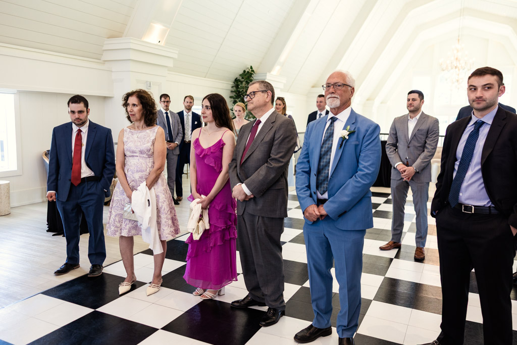 Guests in formal attire watch as bride and groom sign the ketubah during Être Farms wedding celebration