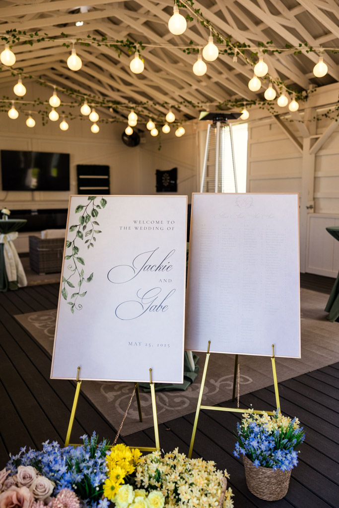 Wedding welcome sign and guest list on easels, surrounded by flowers, under string lights at Être Farms in St. Joseph, Michigan
