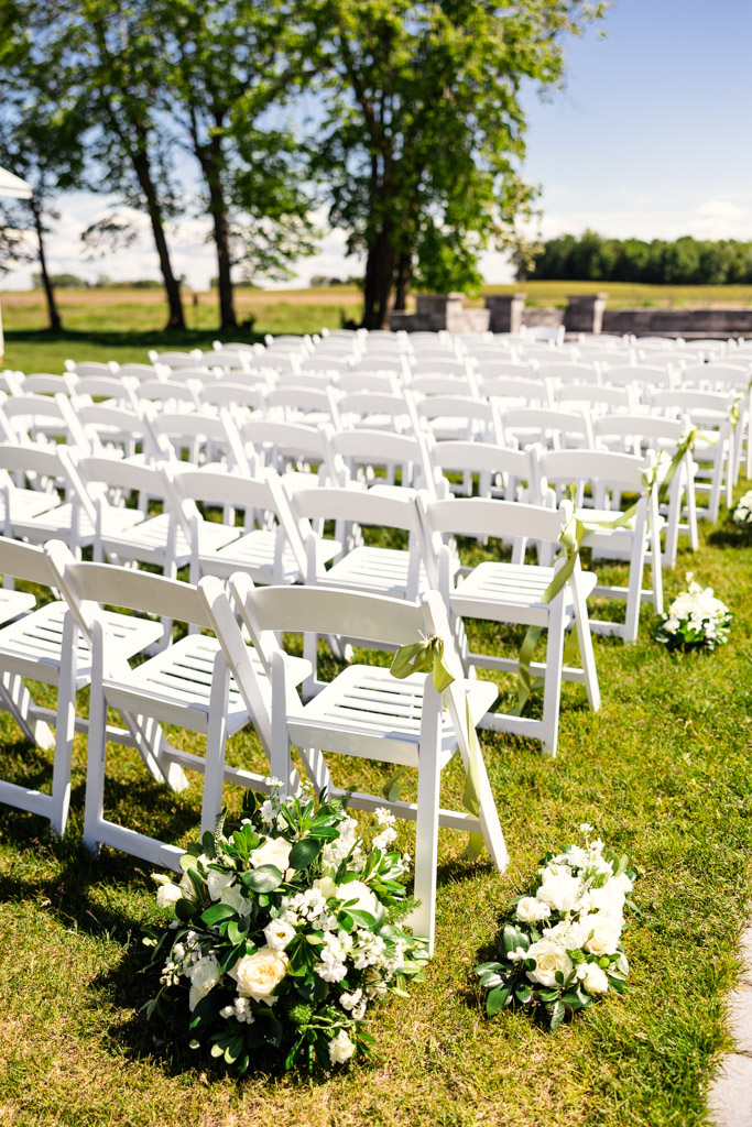 Rows of white chairs and floral arrangements set up outdoors at Être Farms for a wedding ceremony on a sunny day