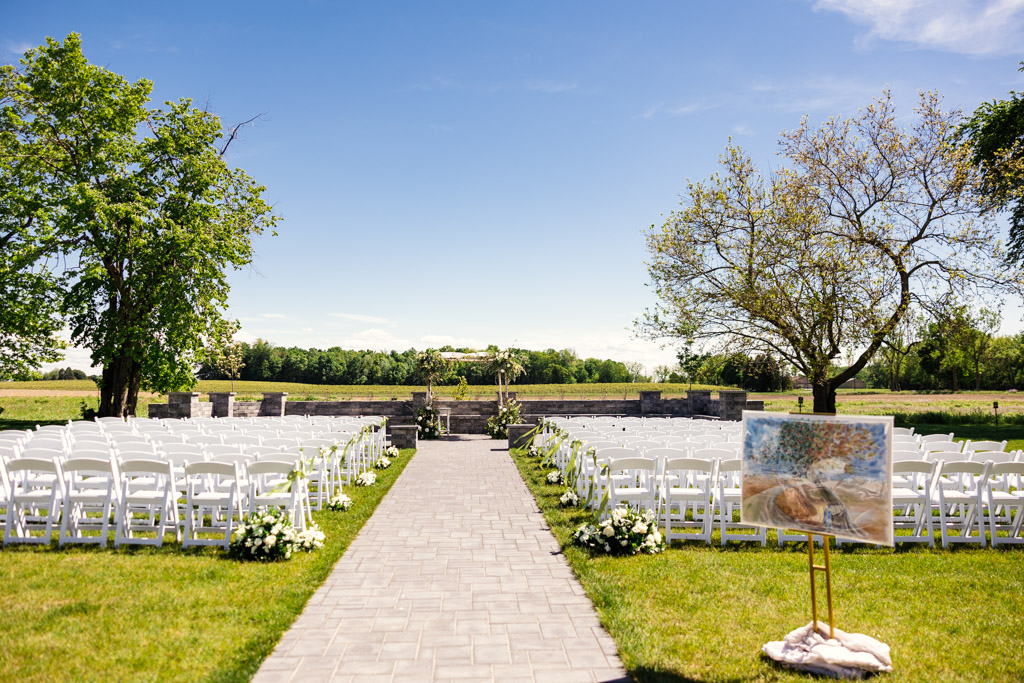Rows of white chairs set up outdoors at Être Farms for a wedding ceremony, with ketubah on an easel by the aisle